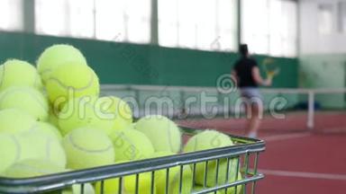 两个年轻人在网球场打网球。前景上装满网球的手推车